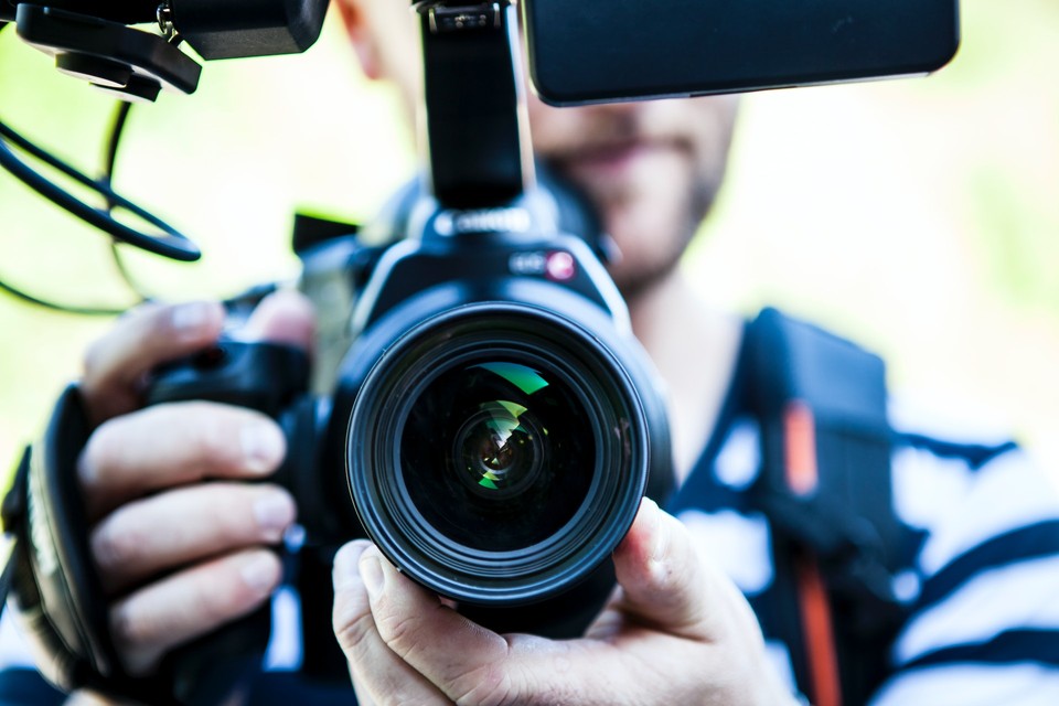 A person holding a professional camera, focusing on the lens