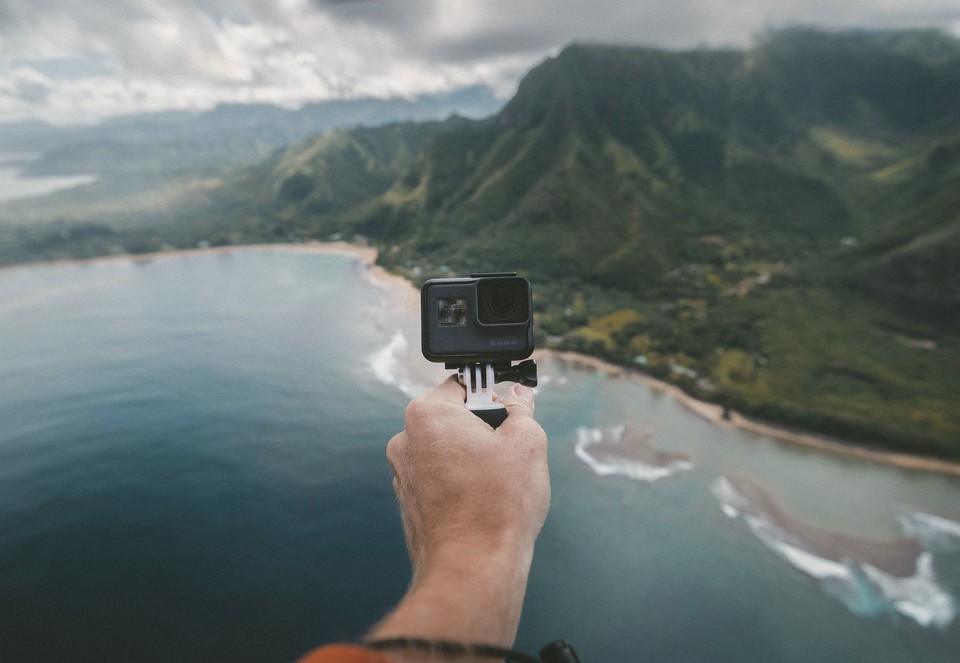 A hand holding a GoPro camera with a scenic background