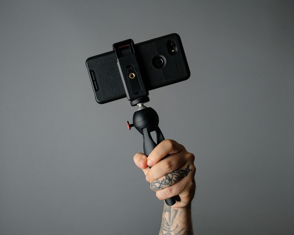 A hand holding a smartphone mounted on a tripod