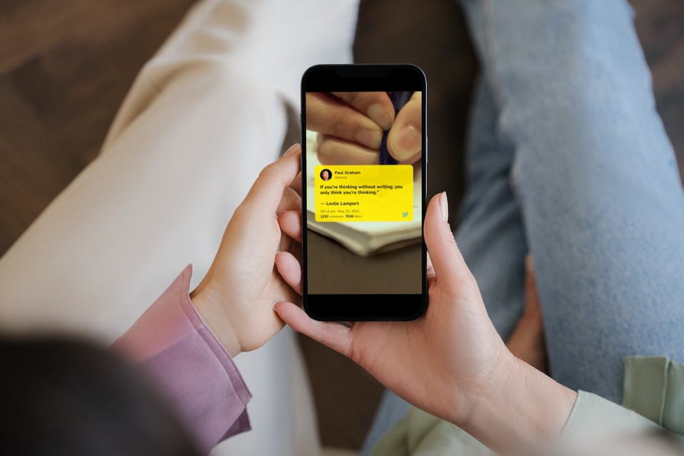 Two people holding a smartphone displaying a tweet video from Paul Graham