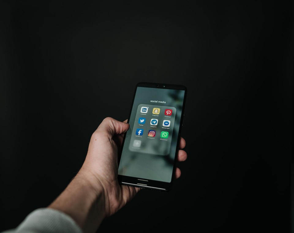 Hand holding a smartphone displaying various social media app icons on the screen