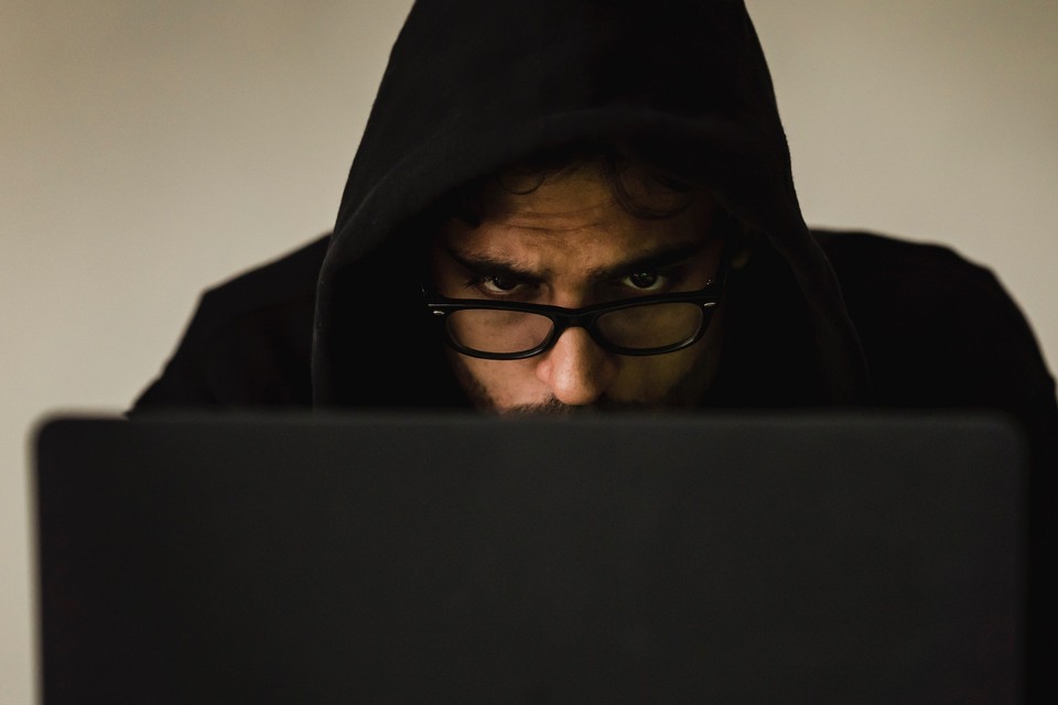 A man wearing a hoodie and glasses, looking intently at a laptop screen