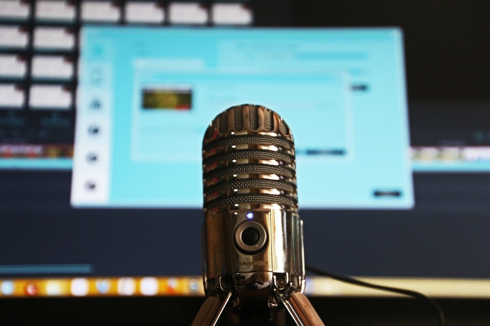 A close-up of a professional microphone with a blurred computer screen in the background