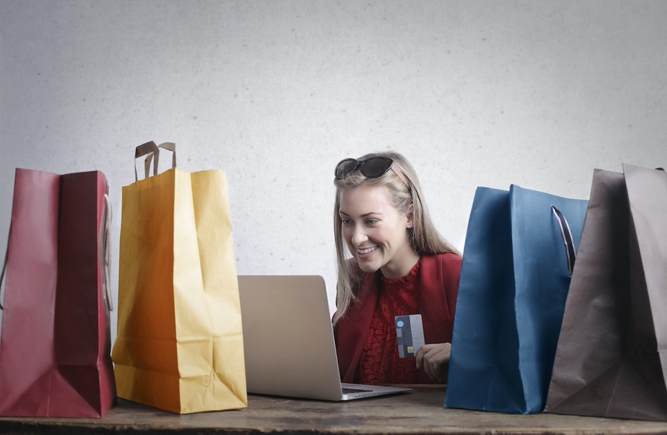 Woman holding a credit card while shopping online on a laptop, surrounded by colorful shopping bags