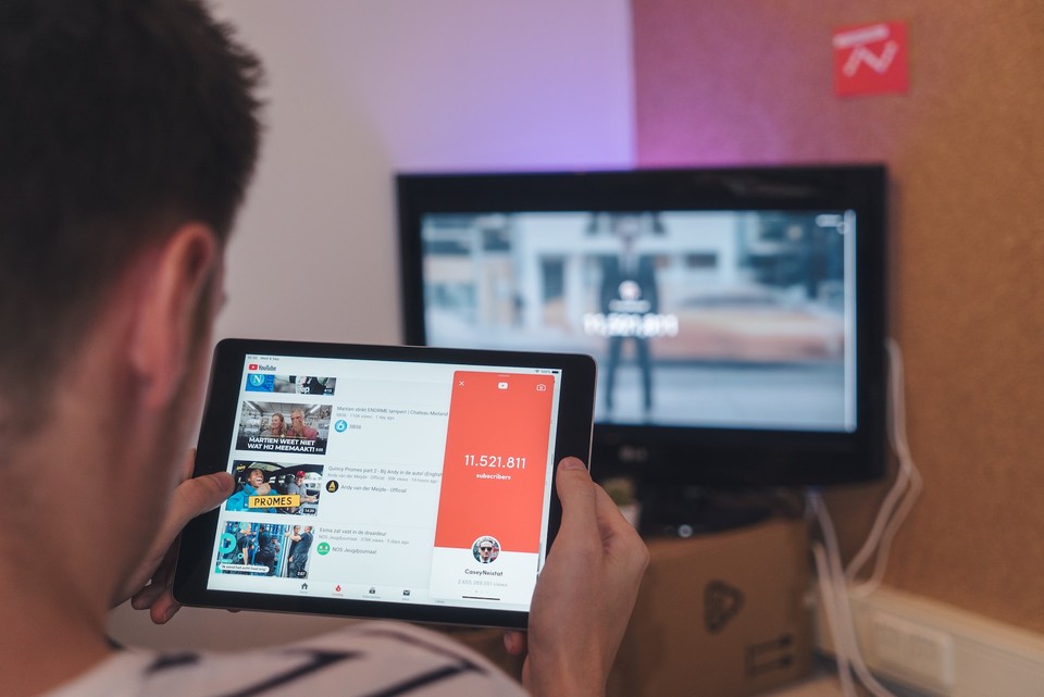 Person using a tablet to view YouTube with a TV in the background